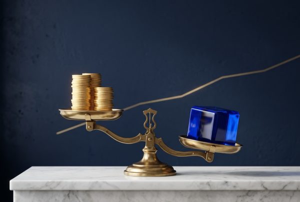 Une balance en laiton : une pile de pièces d'or sur un plateau, un cube de verre bleu plus lourd sur l'autre, devant un mur bleu nuit traversé d'une ligne dorée qui monte.